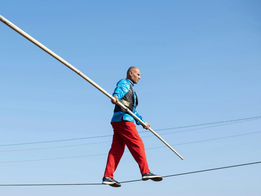 A tightrope walker balancing with a long pole against a clear blue sky